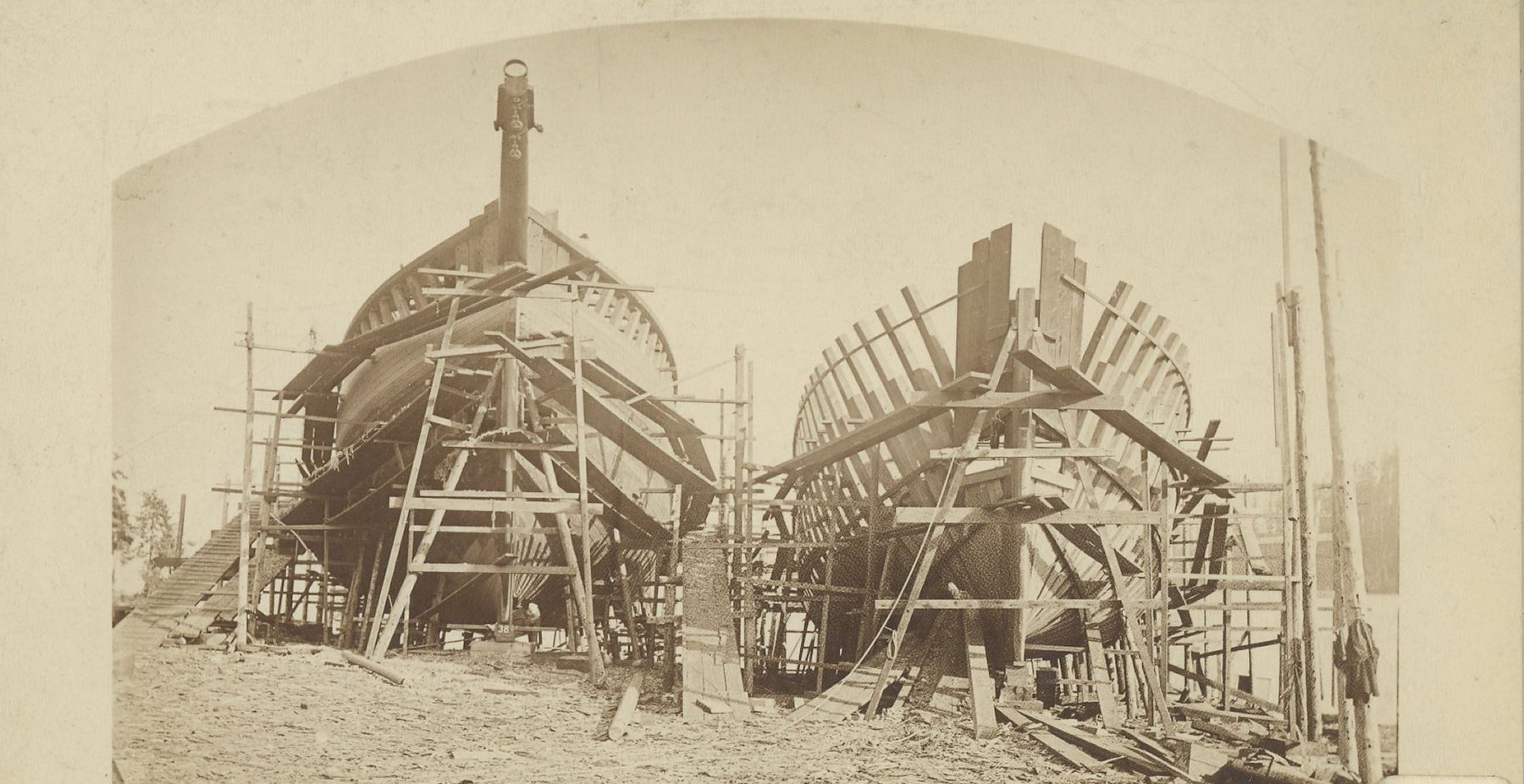 Two large wooden ship hulls under construction, surrounded by scaffolding