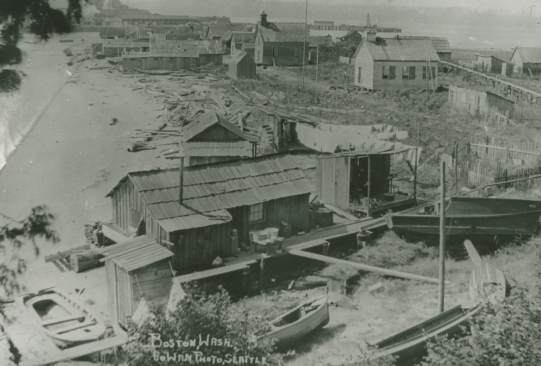 Shake-roofed houses, sheds and small boats along the beach at Little Boston, seen from above