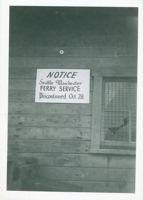 A notice on a wooden wall reading Seattle-Manchester Ferry Service Discontinued Oct. 28