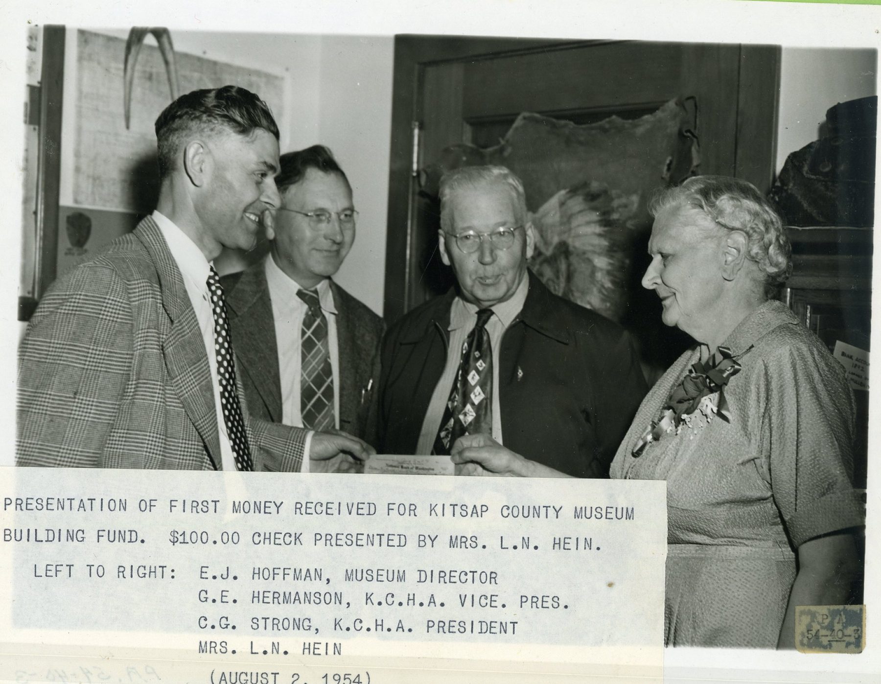 Four people look over a check at a presentation; a typed caption is attached below the photo