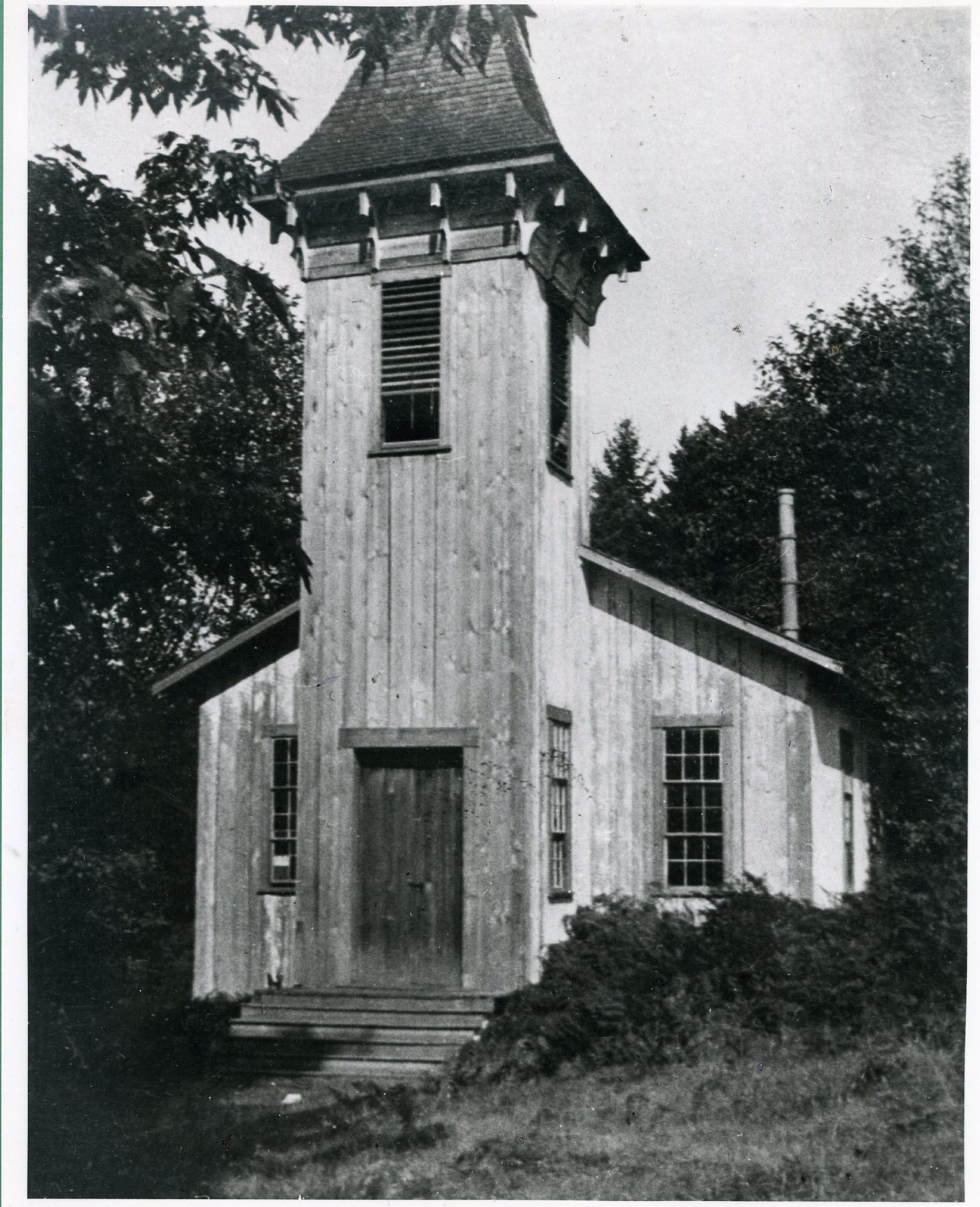 A plain wooden courthouse with a small bell tower, surrounded by trees