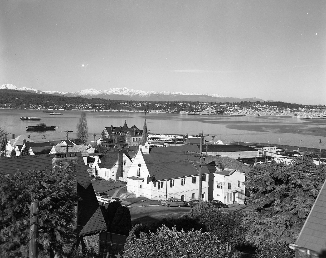 Houses on a hillside above the water, with a town across the bay and the snow-capped Olympic Mountains on the horizon