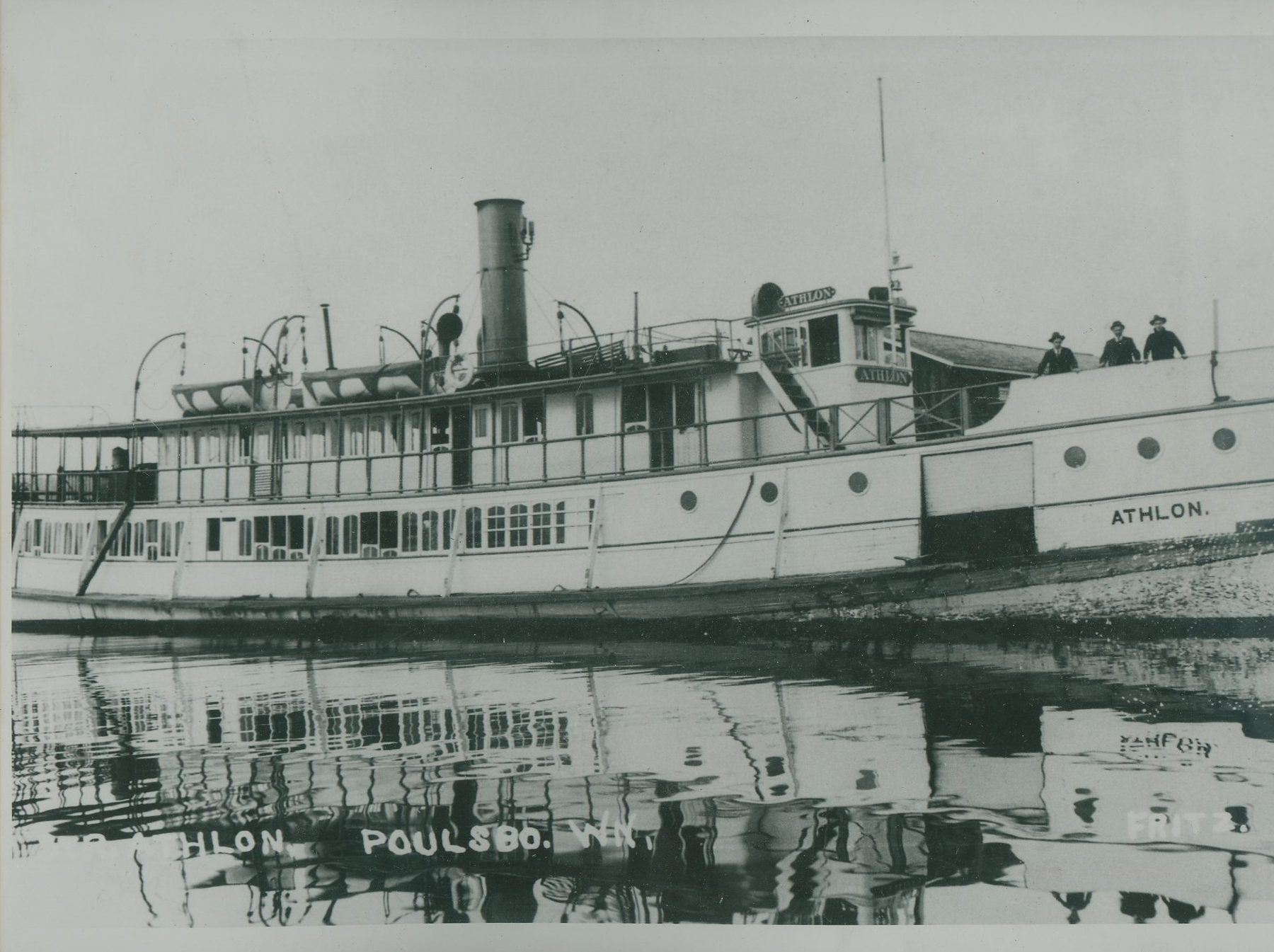 The steamer Athlon at a dock, reflected in still water, with passengers on deck