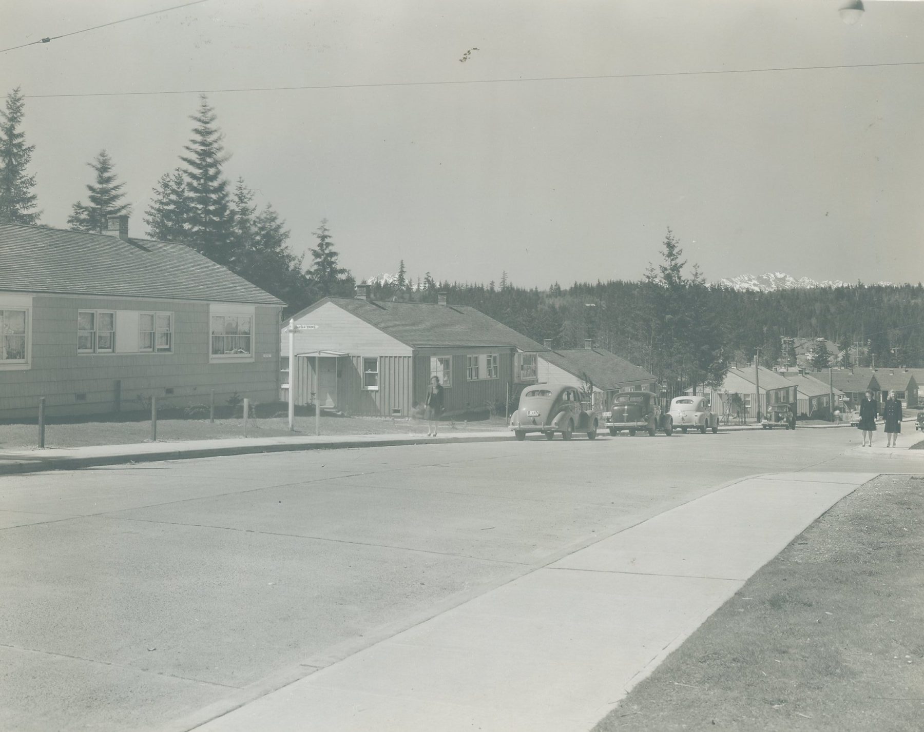 A street of new single-story houses with cars parked along the curb and mountains beyond